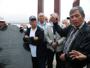 港があった場所に建てられた記念碑前で移民史を説明する城間会長