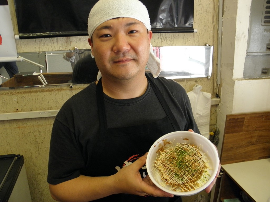 自慢のお好み焼きを手に店主の簗瀬さん