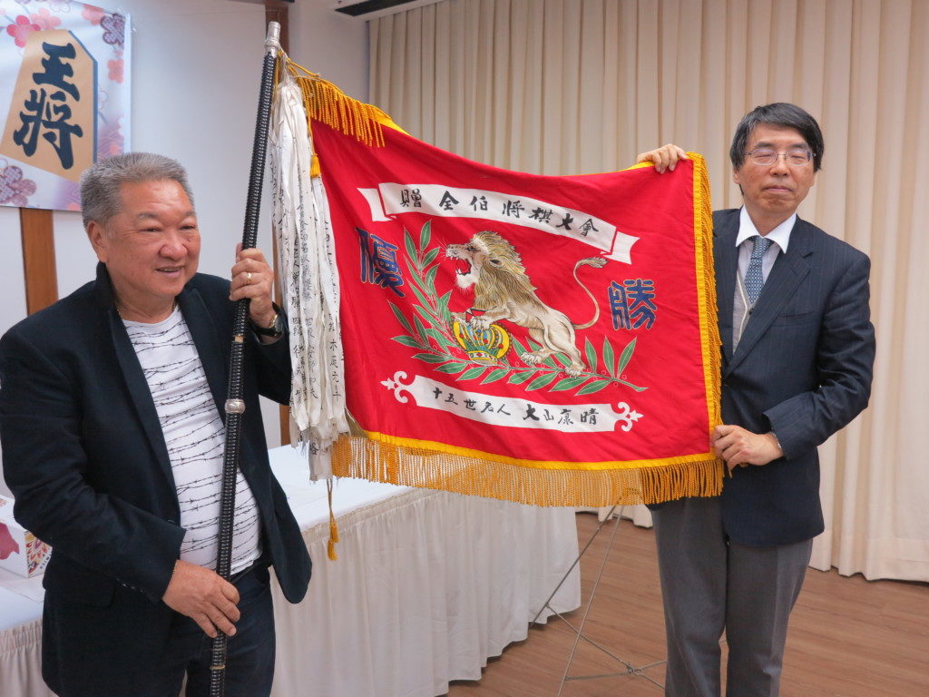 大山康晴氏寄贈の優勝旗を授与する山田大使（右）と高嶋さん（左）