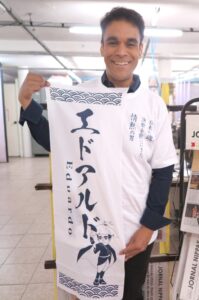 特製Ｔシャツを着て、手ぬぐいを持つエドアルド。「ぜひ応援してください」と笑顔で呼びかけた