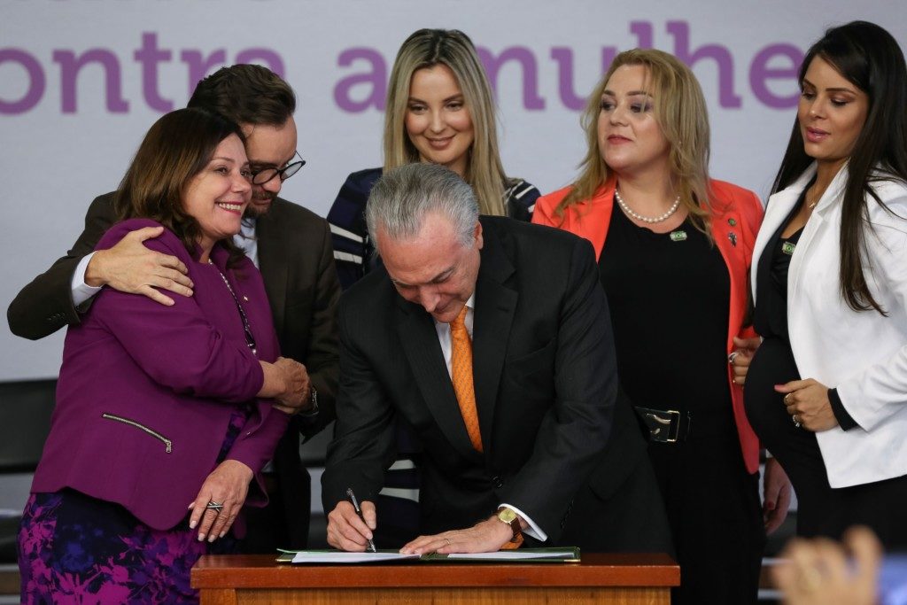 マルセラ夫人や女性議員らに囲まれ、家庭内暴力廃絶計画にサインする大統領（Marcos Corrêa/PR）