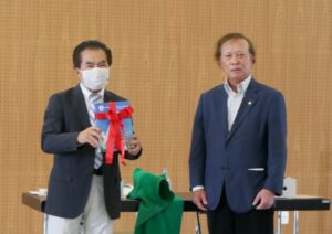 園田副会長から与儀会長へ完成したばかりの６０年史プレゼント